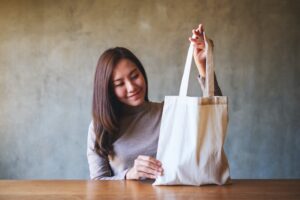 A woman holding and carrying a white fabric tote bag for reusable and environment concept