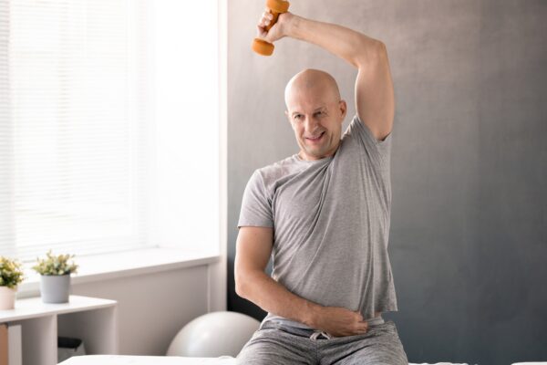 Bald middle aged man in activewear doing physical exercise with dumbbell