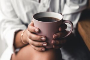 Woman in a white t-shirt holds morning coffee in a pink ceramic cup. Manicure. Front view